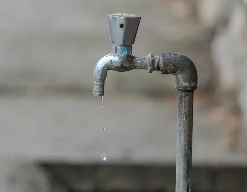 Close-up image of an outdoor water tap with a single droplet falling, highlighting water conservation.